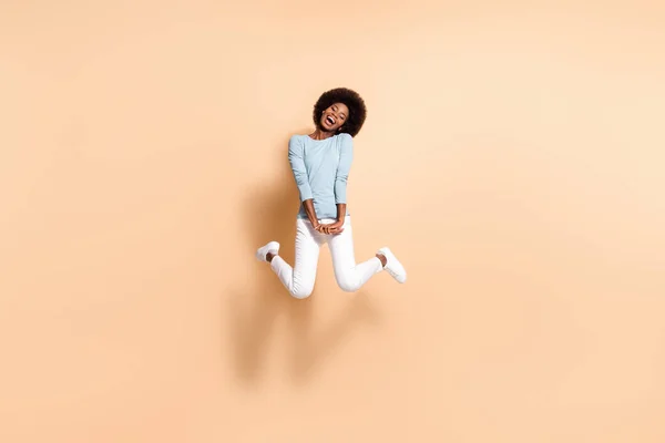 Foto retrato de menina de pele preta segurando duas mãos para baixo pulando no ar isolado no fundo de cor bege pastel — Fotografia de Stock