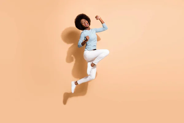 Foto retrato de mulher afro-americana feliz pulando segurando punhos para cima rindo isolado no fundo de cor bege pastel — Fotografia de Stock