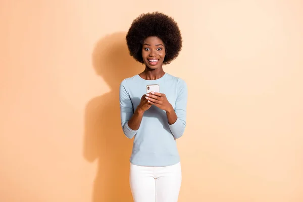 Foto retrato de feliz alegre encaracolado escuro pele menina mantendo celular procurando informações sorrindo isolado no fundo cor bege — Fotografia de Stock