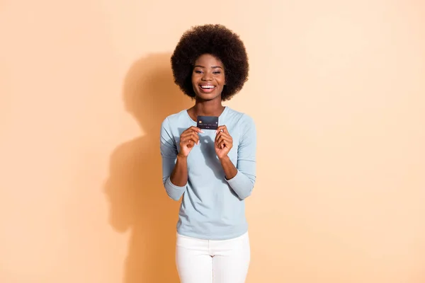 Foto retrato de la niña alegre rizada de piel oscura que muestra la tarjeta bancaria de plástico con camisa azul aislada sobre fondo de color beige — Foto de Stock