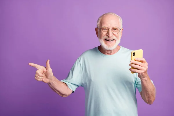鮮やかな紫色の背景に隔離された一方で携帯電話を保持する側に指を指すおじいちゃんの写真の肖像画 — ストック写真