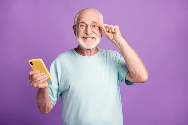 Mutlu bir adamın gözlüğe dokunurken çekilmiş fotoğrafı. Bir elinde telefon, canlı menekşe renkli arka planda izole edilmiş. — Stok fotoğraf