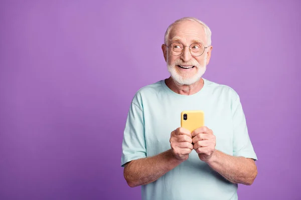 İki eliyle telefonu tutan yaşlı bir adamın fotoğrafı. Mor renkli arka planda izole edilmiş boş bir alana bakıyor. — Stok fotoğraf