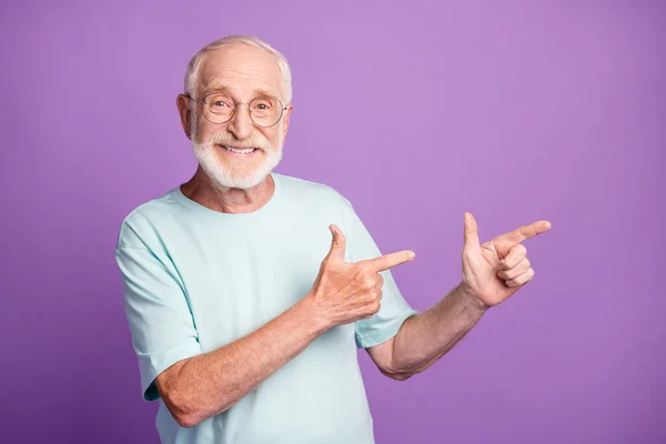 Porträtt av glad rolig gammal man regissera tomt utrymme bära glasögon blå t-shirt isolerad över lila färg bakgrund — Stockfoto