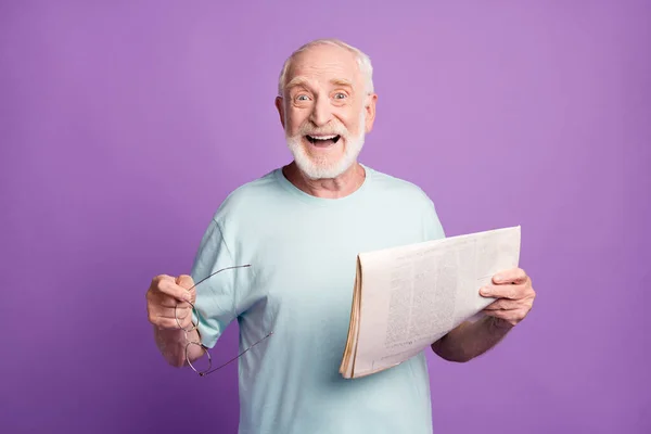 Retrato de feliz sonriente pelo gris barba pensionista celebrar gafas periódico usar luz azul camiseta aislado en violar fondo — Foto de Stock