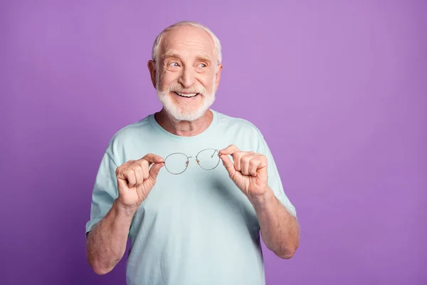 Foto av glad gammal man tittar tomt utrymme hålla glasögon isolerade över violett färg bakgrund — Stockfoto