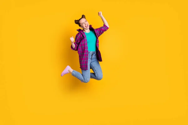 Полная длина фото привлекательной сумасшедшей взволнованной девушки подростка прыгать с воздуха поддержки спортивной команды поднять кулаки кричать цели приветствия носить повседневную клетчатую рубашку обувь джинсы изолированный желтый цвет фона — стоковое фото