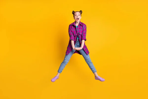 Фотографія повного розміру досить фанк-божевільна збуджена дівчина-підліток підстрибує гарний настрій радіючи поширеним ногам літні вихідні носять повсякденні сорочки кросівки джинси ізольовані жовтого кольору фону — стокове фото