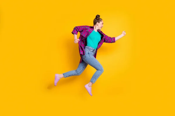 Full kropp profil foto av attraktiv tonåring dam hoppa högt upp springa race maraton glada att vinna rusa konkurrens bära casual rutig skjorta sneakers jeans isolerad gul färg bakgrund — Stockfoto