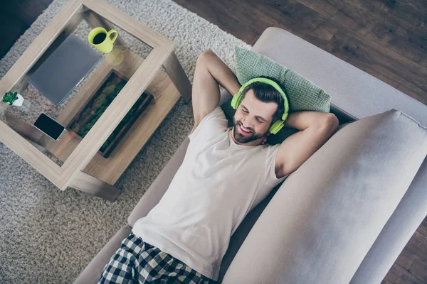 Alto ángulo arriba ver foto de chico guapo doméstico quedarse en casa tiempo de cuarentena tumbado acogedor sofá daydream escuchar disfrutar de los auriculares modernos sala de estar interior moderno en interiores — Foto de Stock