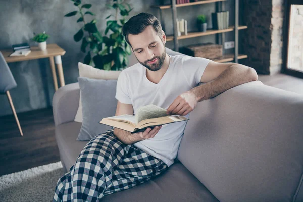 Foto van gerichte man zitten divan hebben corona virus quarantaine vakantie lees boek dragen geruite plaid broek wit t-shirt in huis binnen — Stockfoto