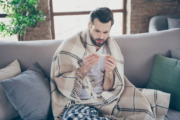 Retrato de su agradable chico atractivo enfermo sentirse mal licencia enferma sentado en diván medición de temperatura sufrimiento captura fría temporada de invierno en el loft moderno estilo interior industrial en interiores — Foto de Stock