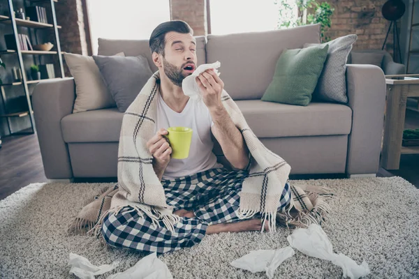 Foto de chico guapo hogareño sentarse piso sofá cuarentena estancia casa cubierta manta bebida medicina caliente bebida estornudos papel servilleta malestar corona virus pijama sala de estar interior — Foto de Stock