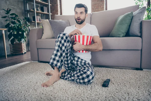 Omg, ¿qué es? hombre asombrado han cuarentena tiempo libre ver película impresionado suspenso inesperado final celebrar grande rojo rayas caja de maíz sentarse alfombra en casa en el interior — Foto de Stock