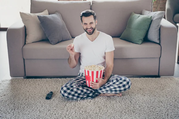 Retrato de su agradable atractivo alegre alegre morena chico sentado en la alfombra viendo series de televisión comer maíz divertirse fin de semana en el loft moderno casa interior industrial apartamento — Foto de Stock