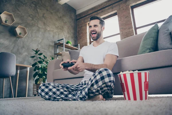 Low angle view portret van zijn he nice nice cheerful cheery blij brunet guy sitting on carpet playing online game having fun at modern loft brick industrial interior house flat apartment — Stockfoto