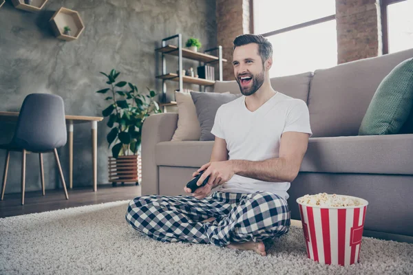 Retrato de su agradable atractivo emocionado alegre alegre alegre chico sentado en la alfombra jugando juego en línea divertirse tiempo libre comer maíz pop en el estilo interior industrial loft moderno — Foto de Stock