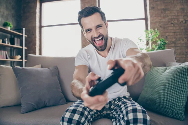 Portrait of his he nice attractive excited overjoyed cheerful cheery guy sitting on divan playing online game having fun spending weekend free time at modern loft industrial interior style — Stock Photo, Image