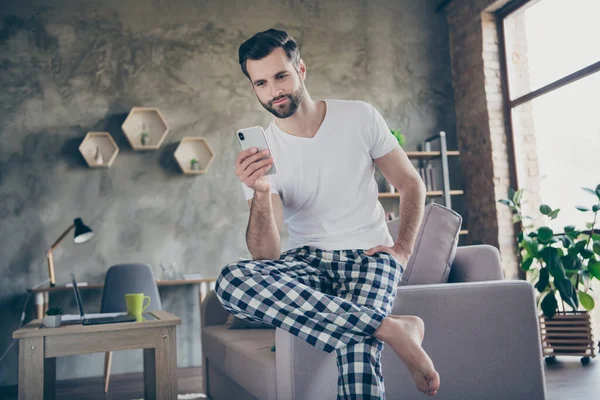 Portrait de son il beau gars brunet concentré attrayant assis sur le canapé à l'aide d'un appareil numérique bavarder auto-isolement à loft moderne brique industrielle intérieur maison appartement — Photo