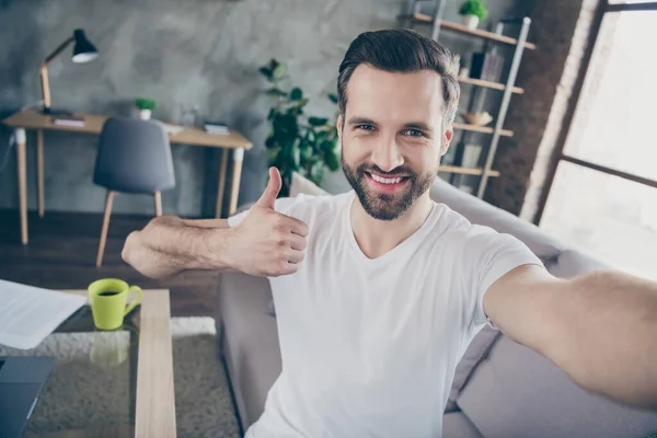 Autorretrato de su agradable atractivo alegre alegre chico que gerente sentado en diván trabajando remotamente en línea mostrando anuncio de pulgar solución de anuncio fresco en el estilo interior industrial loft moderno — Foto de Stock