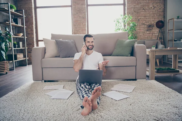 Foto de hombre positivo gerente de marketing sentarse alfombra trabajo remoto portátil llamada teléfono inteligente colega amigo decir hablar decir hablar covid-19 noticias de puesta en marcha en casa en interiores — Foto de Stock