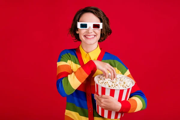 Foto van aantrekkelijke grappige dame houden grote popcorn emmer eten zoute zoete maïs bekijk film bioscoop première door middel van 3d specs dragen gestreept vest trui geïsoleerde heldere rode kleur achtergrond — Stockfoto