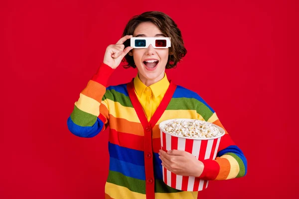 Bild av ganska rolig dam hålla stora popcorn hink titta på film premiär trevlig bild kvalitet slitage 3d glasögon randig kofta hoppare isolerad ljus röd färg bakgrund — Stockfoto