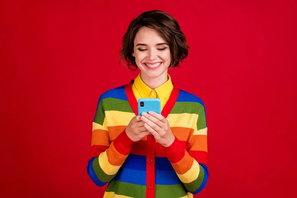 Foto de hermosa señora lesbiana bastante sostener las manos del teléfono leyendo novia sms agradables sentimientos alegres sonrisa dentada desgaste rayas jersey cárdigan aislado color rojo fondo —  Fotos de Stock