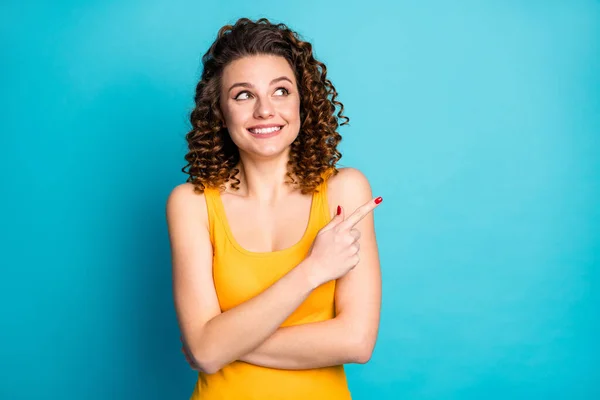 Foto de linda linda menina ruiva sonhadora olhar animado direcionando dedo vazio espaço desgaste amarelo tanque-top isolado azul cor de fundo — Fotografia de Stock