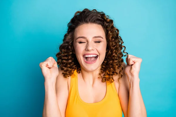 Foto von lustigen rothaarigen jungen Mädchen heben die Fäuste, schließen Augen, Mund aufgeregt tragen gelben Tank-Top isoliert blaue Farbe Hintergrund — Stockfoto