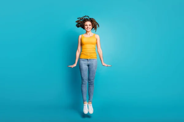 Photo of funky lady energetic person jump high up air flight wear casual yellow singlet jeans shoes blue color background — Stock Photo, Image