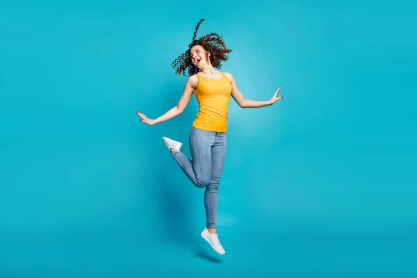 Foto av vackra dam hoppa hög glädje helgdagar bära casual gul singlet topp jeans skor isolerad blå färg bakgrund — Stockfoto