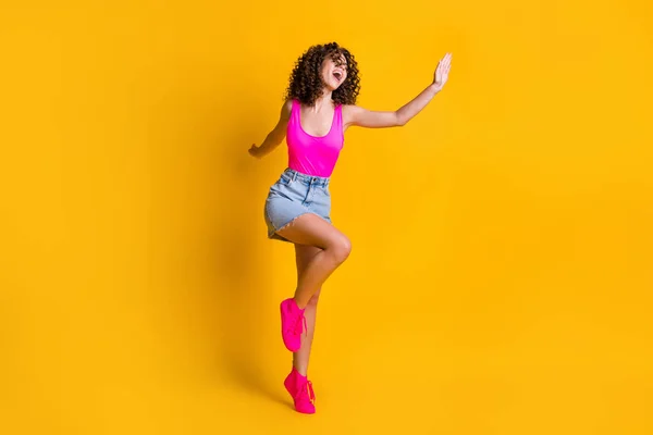 Full längd profil foto av attraktiva unga lockigt dam dans disco studenter fest mager figur bära rosa tank topp denim mini kjol skor isolerad ljus gul färg bakgrund — Stockfoto