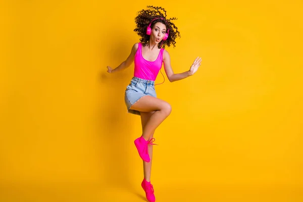 魅力的な巻き女性ジャンプダンスのフル長さの写真学生パーティー喜んで耳を傾けるイヤフォン音楽を着用ピンクタンクトップデニムミニスカートの靴孤立明るい黄色の色の背景 — ストック写真