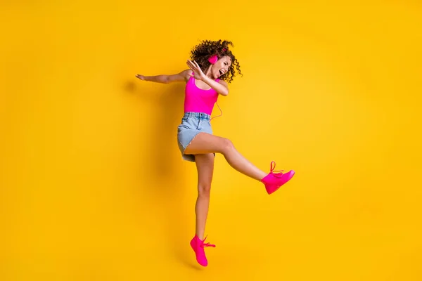 Full body profile photo of charming crazy lady jump high carefree listen earphones modern technology dancing dab wear pink tank top mini skirt shoes isolated bright yellow color background
