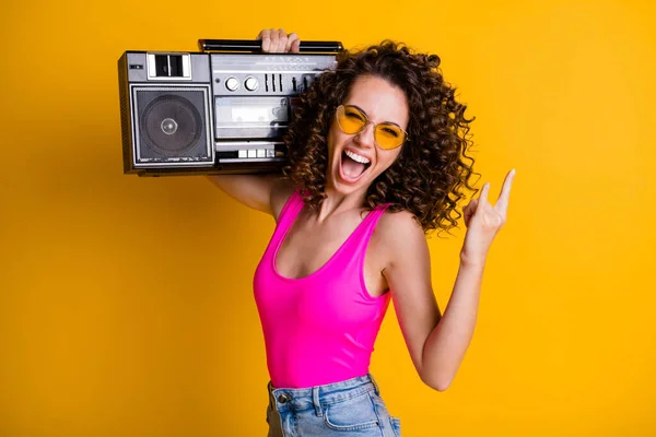 Bild av cool galen ung dam vågig frisyr lyssna ungdoms musik hålla retro boom box chill beach party gör finger horn bära sommar rosa singlet isolerad levande gul färg bakgrund — Stockfoto