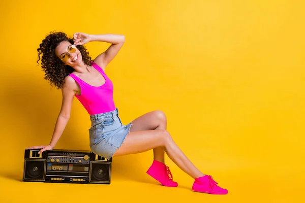 Full body profile photo of charming lady sit retro boom box holiday party entertain posing photographing wear sun specs pink singlet denim skirt shoes isolated shine yellow color background