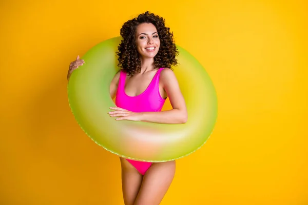 Foto retrato de una chica morena rizada sosteniendo un círculo de natación verde inflable usando ropa de baño fucsia aislada sobre un fondo de color amarillo vivo — Foto de Stock