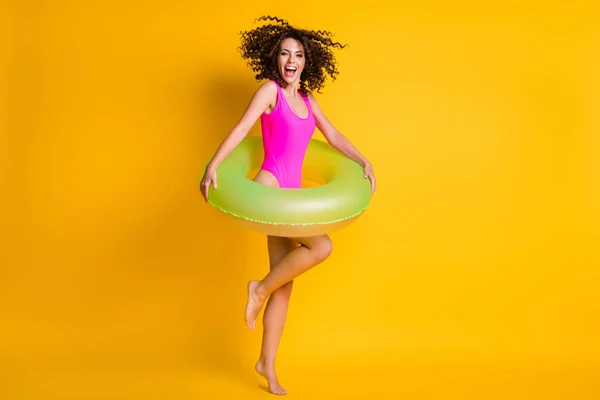 Photo portrait of happy brunette girl jumping up standing on one leg holding green inflatable ring isolated on vivid yellow colored background — Stock Photo, Image