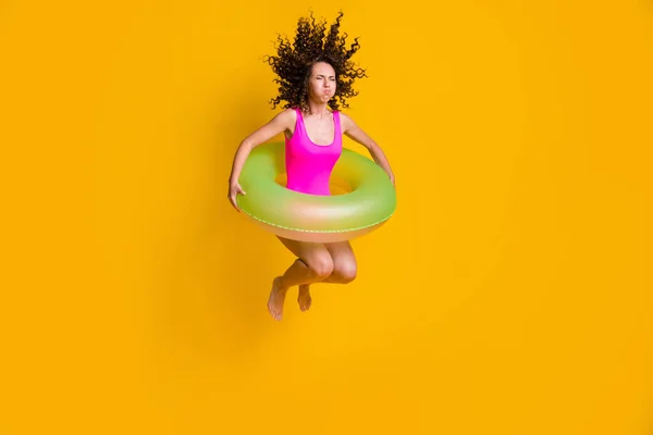 Фотографічний портрет молодої кучерявої дівчини, що стрибає в басейн, тримаючи дихання закритими очима з надувним зеленим колом, одягненим у фуксію, що плаває, ізольований на яскраво-жовтому фоні — стокове фото