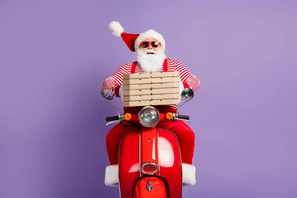 Fénykép vicces Mikulás lovagolni gyors moped hold pizza dobozok viselnek x-mas jelmez csíkos ing sapka szemüveg elszigetelt ibolya szín háttér — Stock Fotó