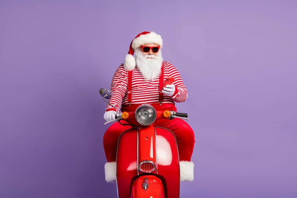 Foto van vrolijke santa rijden fiets houden telefoon look scherm slijtage x-mas kostuum cap zonneglas geïsoleerde paarse kleur achtergrond — Stockfoto