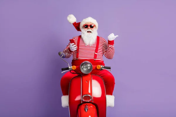 Foto van santa drive fiets houden telefoon directe vinger lege ruimte slijtage x-mas kostuum cap zonneglas geïsoleerde paarse kleur achtergrond — Stockfoto