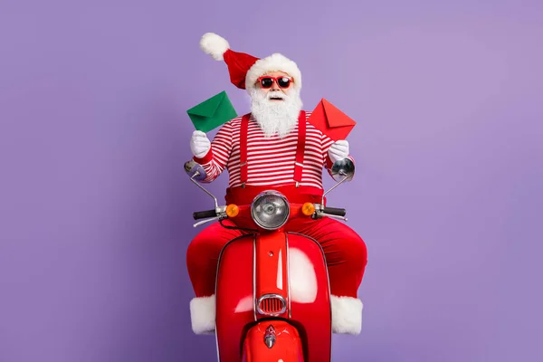 Foto santa ride moped mendemonstrasikan dua amplop mengenakan kostum x-mas kacamata kacamata kacamata terisolasi latar belakang warna ungu — Stok Foto