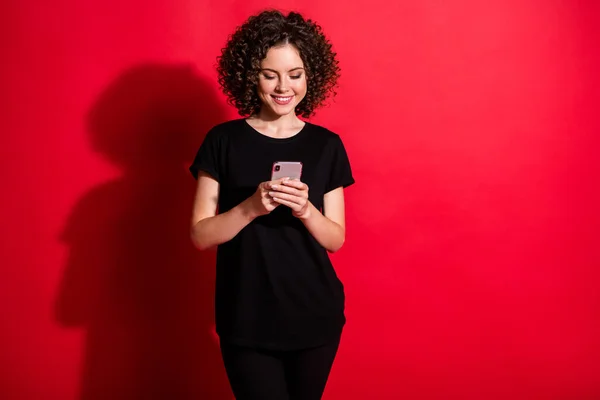 Foto de adorable mujer rizada brillante desgaste casual traje negro buscando mensajes de texto teléfono aislado color rojo fondo —  Fotos de Stock