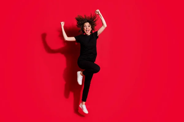 Foto ritratto vista corpo pieno di ragazza che celebra con pugni in aria saltando isolato su sfondo rosso vivido — Foto Stock