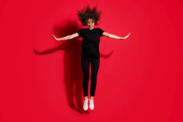 밝은 빨간색 배경에 손을 따로 떼고 행복 한 소녀가 양 옆으로 뛰어오르는 모습의 전체 사진 — 스톡 사진
