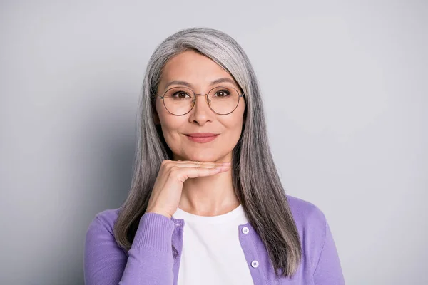 Foto de encantadora linda señora madura mano palma barbilla tímida sonrisa procedimiento desgaste gafas gafas blanco camisa violeta cárdigan aislado gris color fondo —  Fotos de Stock