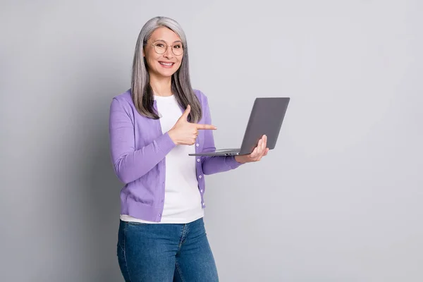 Portrait photo d'une vieille femme souriante amicale et satisfaite pointant sur un ordinateur portable avec un doigt isolé sur un fond de couleur grise — Photo