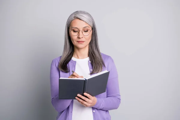 Foto de retrato de una anciana empresaria concentrada anotando notas en el organizador con anteojos aislados sobre fondo de color gris — Foto de Stock